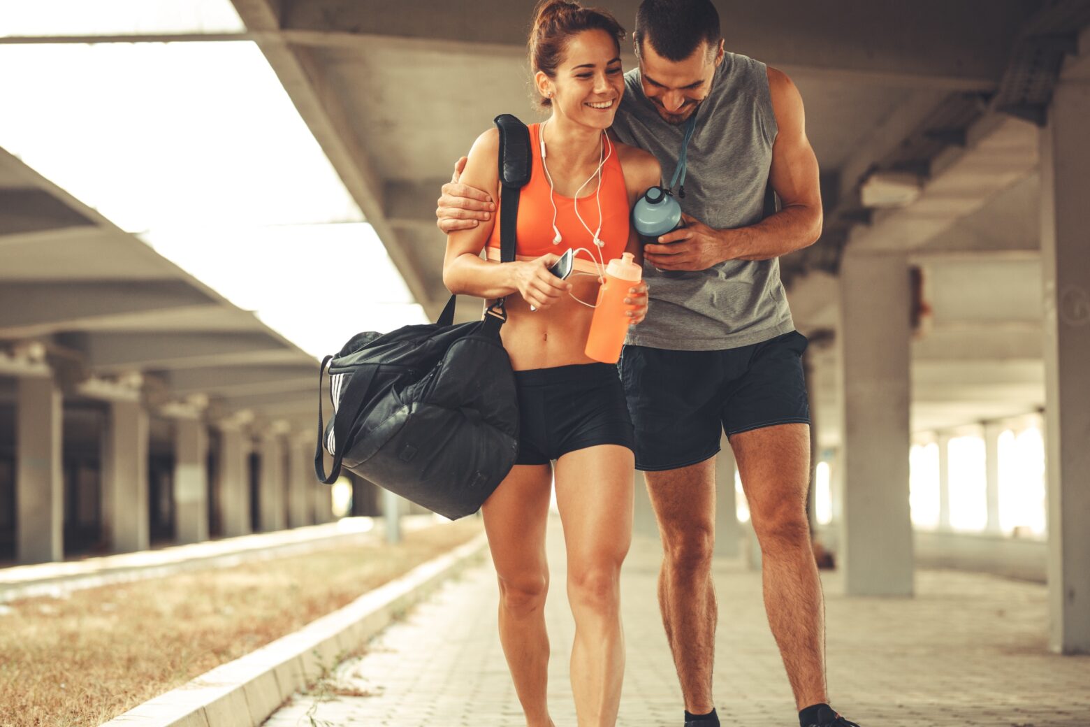 A happy athletic couple walking underneath bridge in an urban area, heading to the gym.