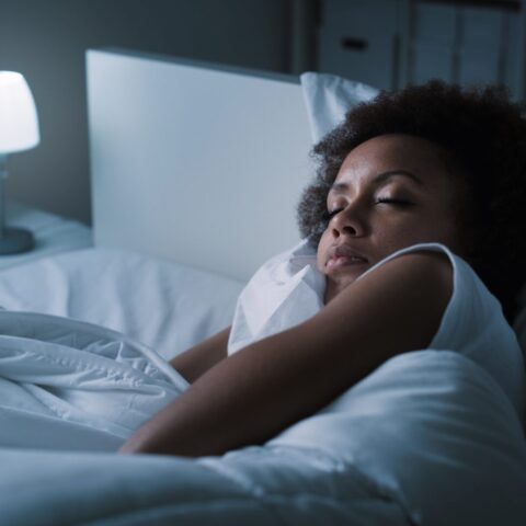 Woman sleeping in bed with small light on nightstand.