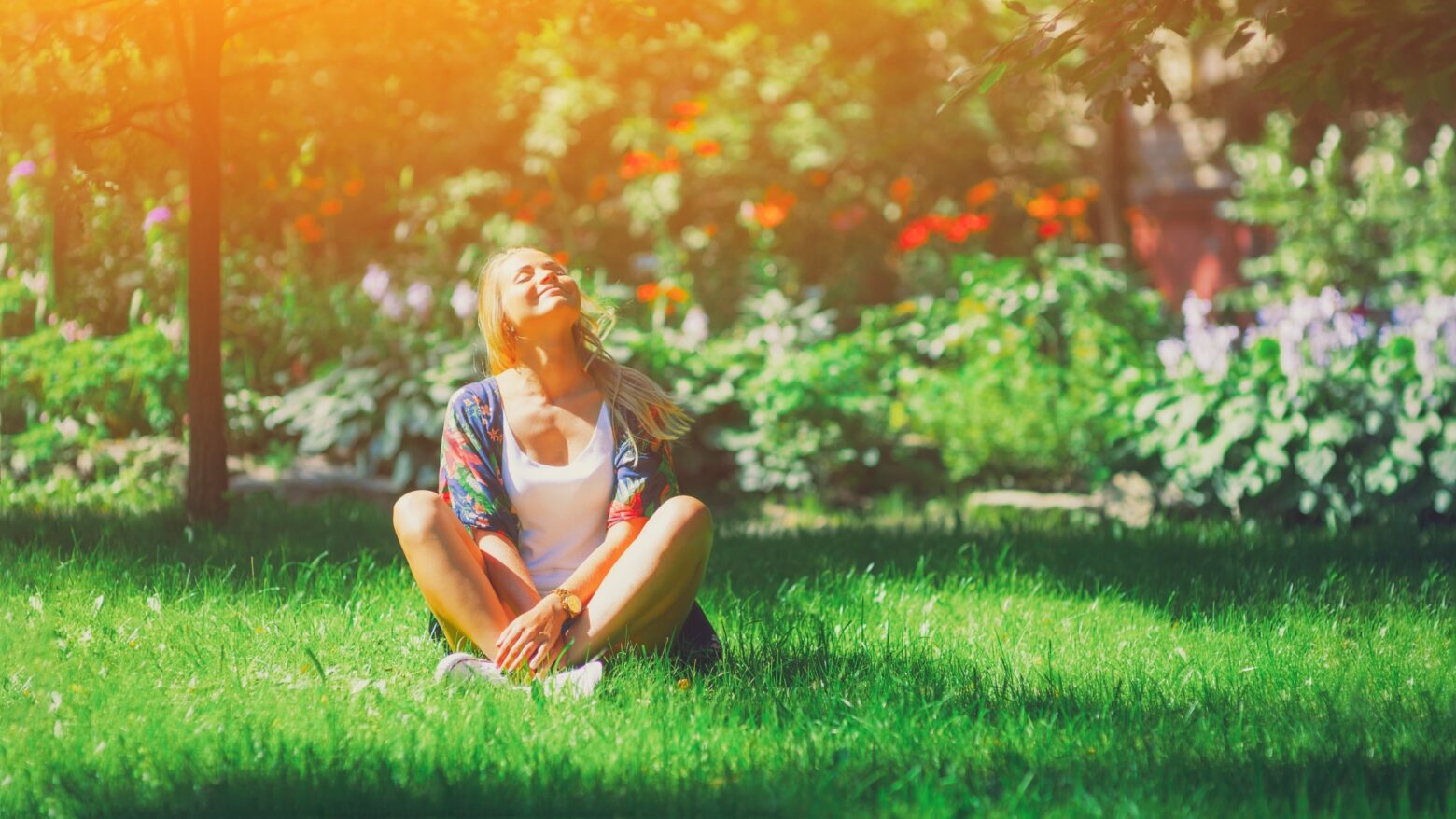 A young woman sits in a grassy park, basking in the sunshine