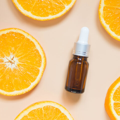 A spray bottle of vitamin C serum for skin health next to oranges