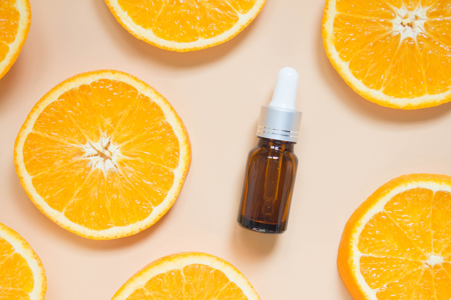 A spray bottle of vitamin C serum for skin health next to oranges