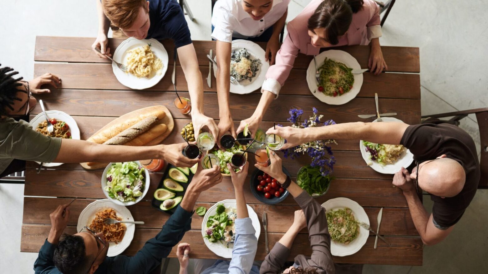 A group of people cheers over a dining table full of food.