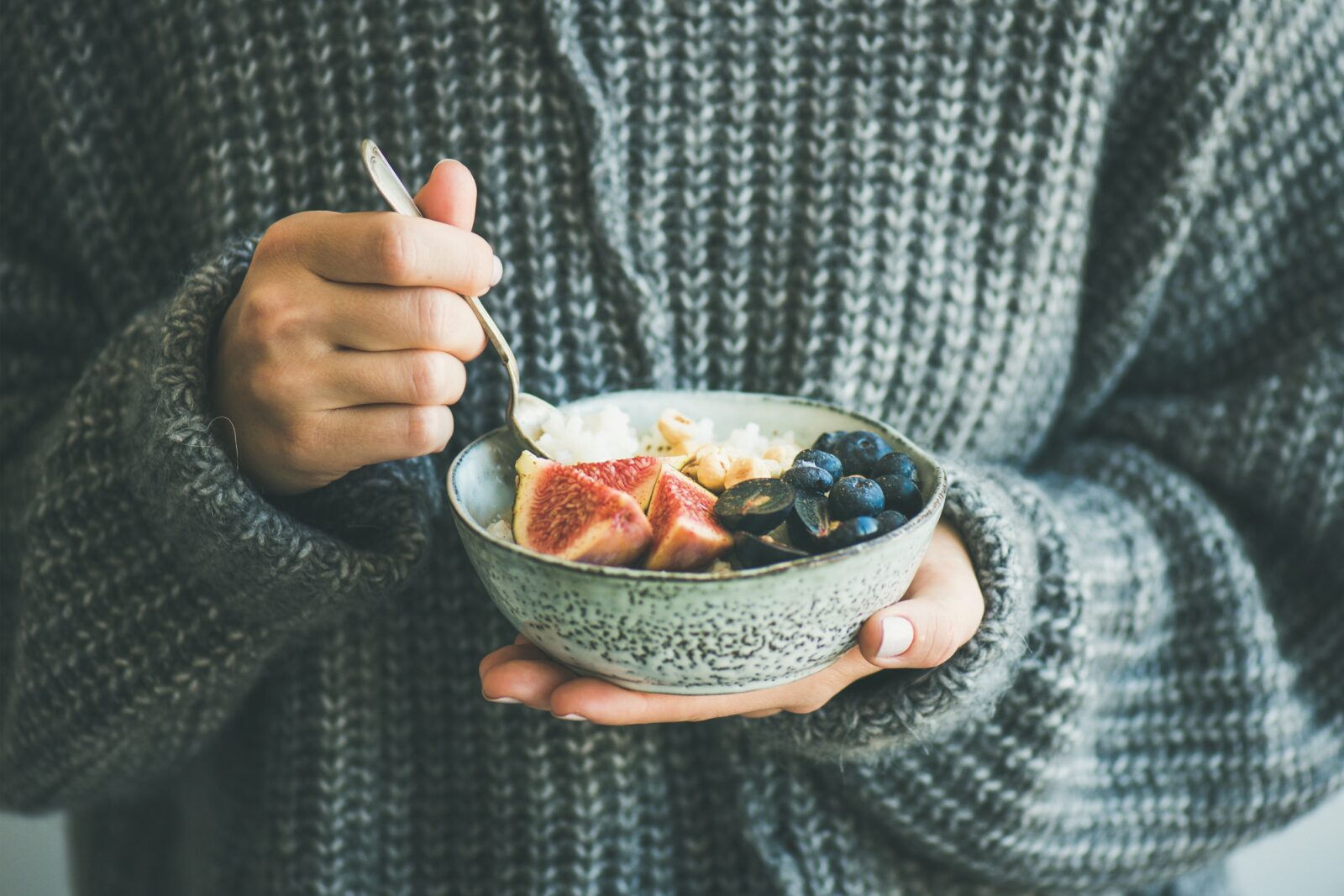 Someone in a sweater eating a bowl of fruit.