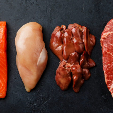 Raw cuts of salmon, chicken, steak, and organ meat on black slate