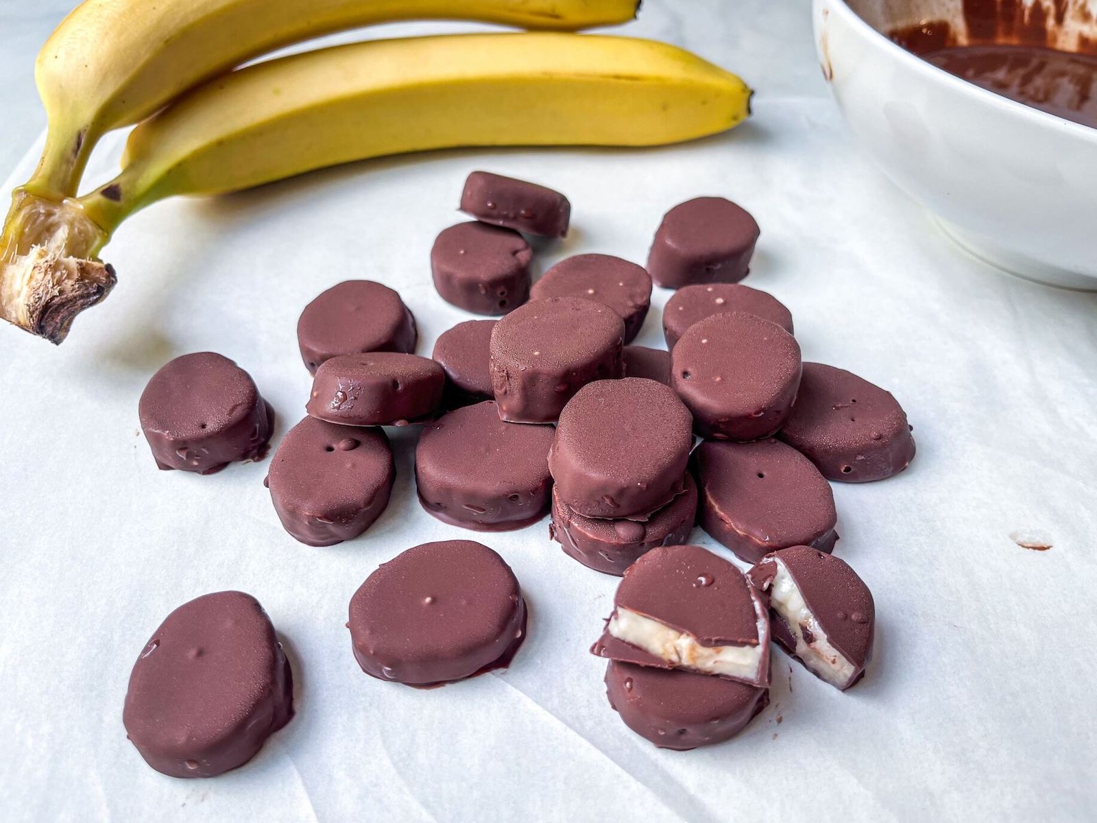 Chocolate covered banana bites sitting on parachment paper.