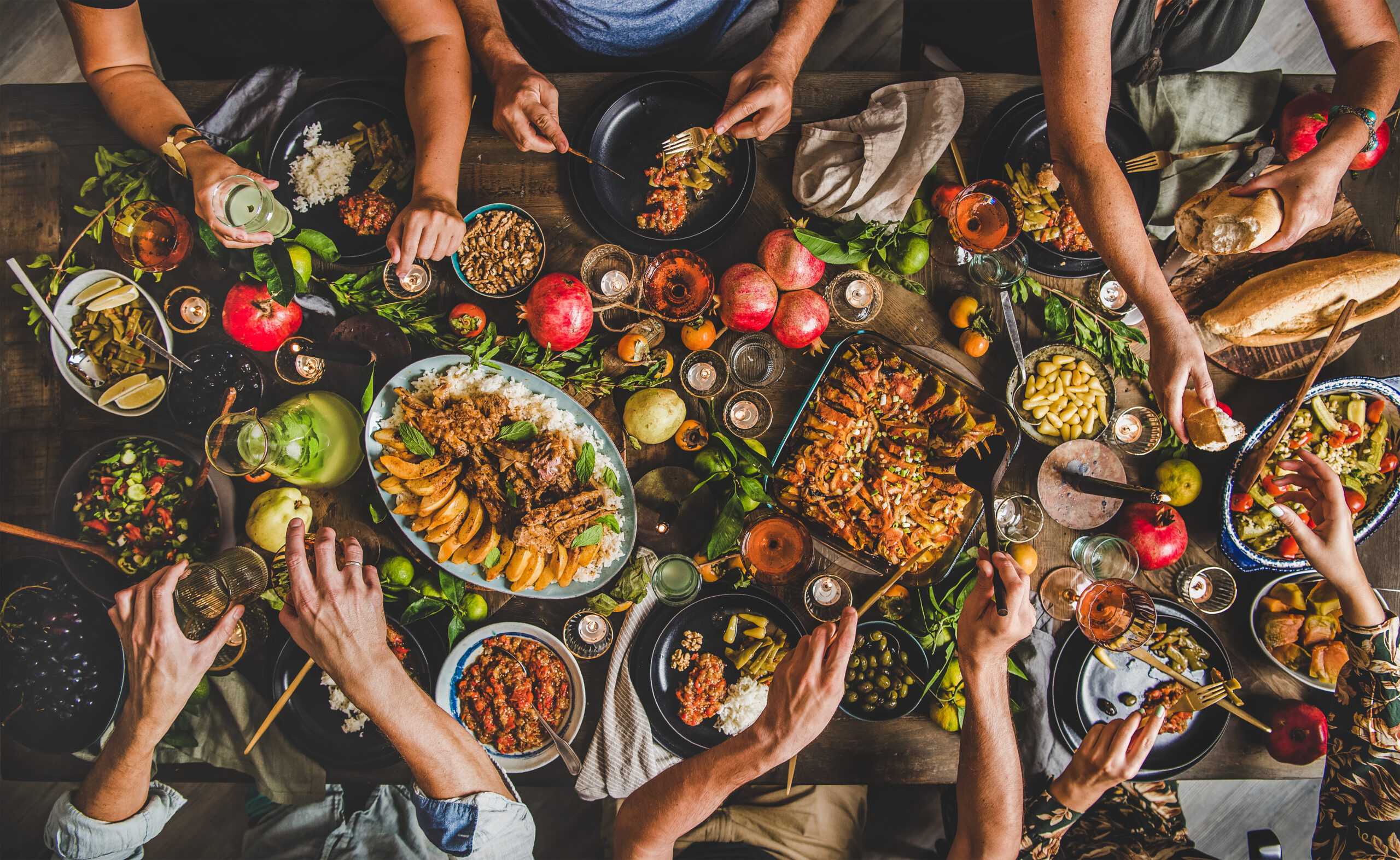 A gathering of friends and family around a dinner table, shot from above to show a huge spread of a variety of foods.