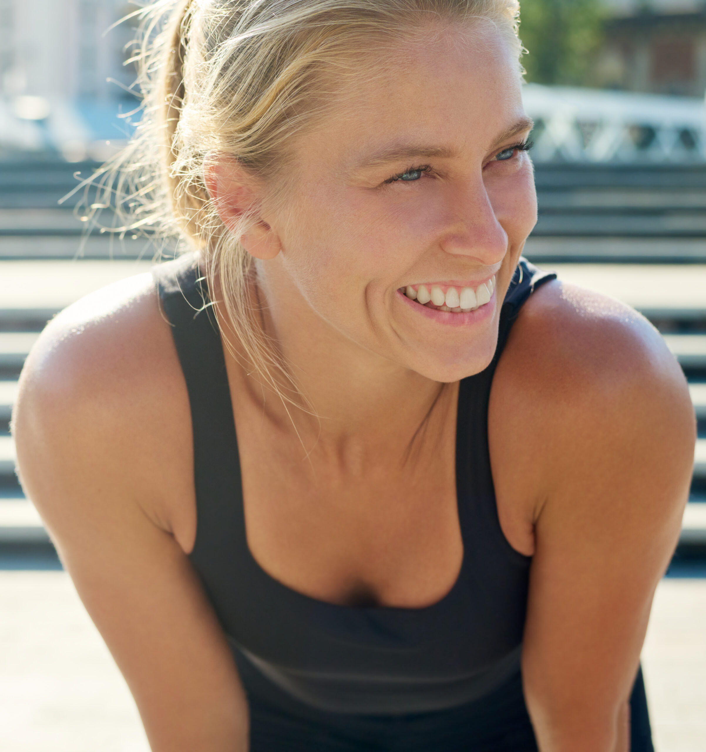 A cheerful blond sportswoman in black activewear enjoying break after outdoor sports training