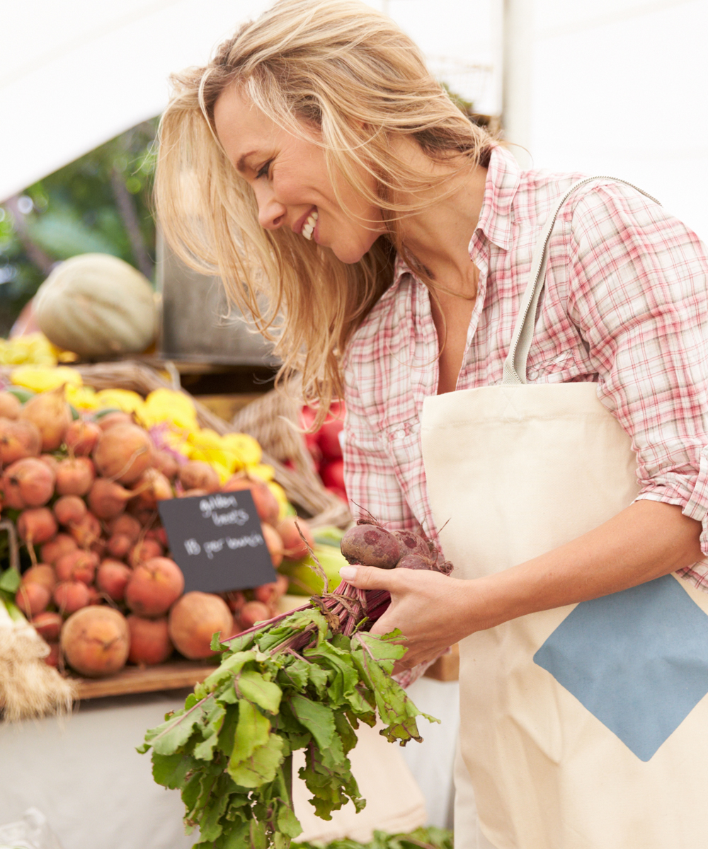 A middle-aged blonde woman shops for vegetables at the farmer's market.