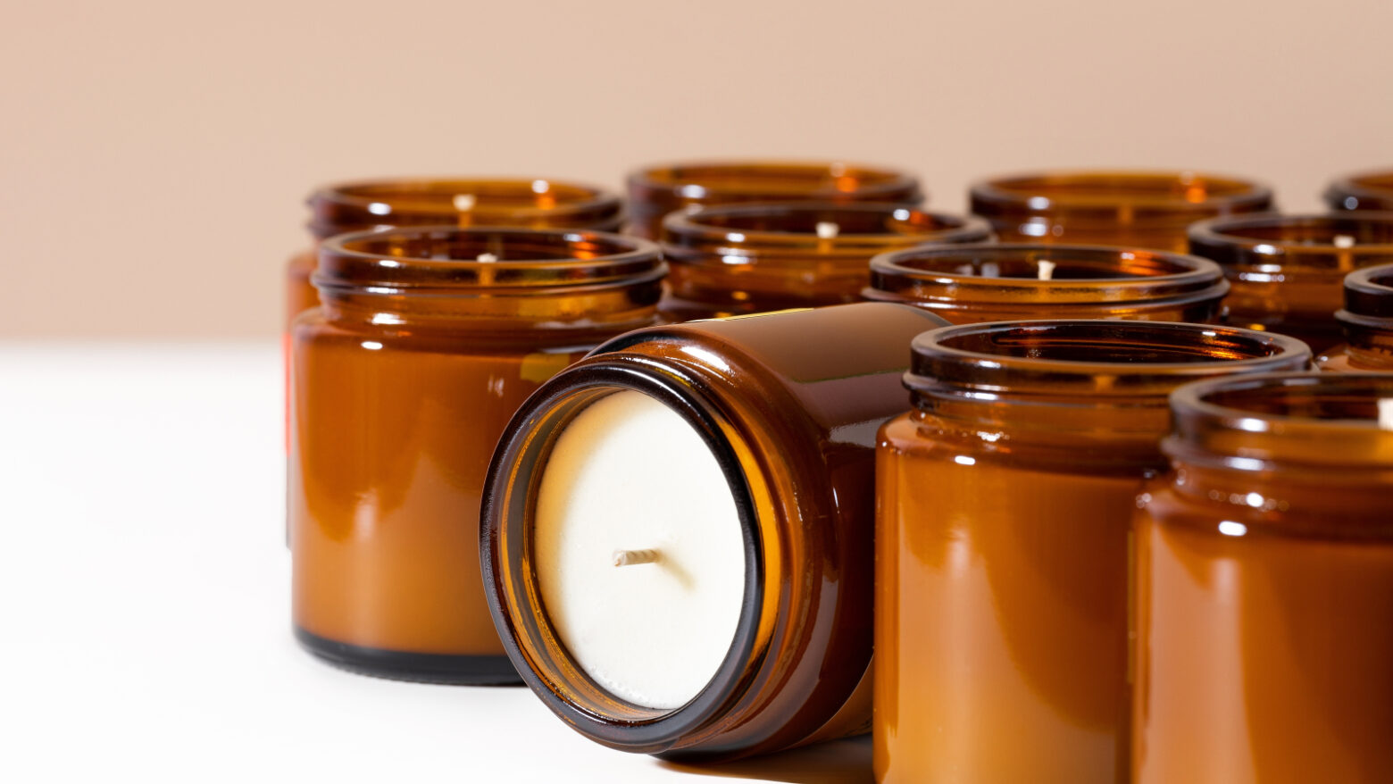 Rows of candles in glass amber jars, with one candle tipped on its side to show the wick