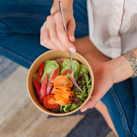 Woman eating a salad out of a paper bowl