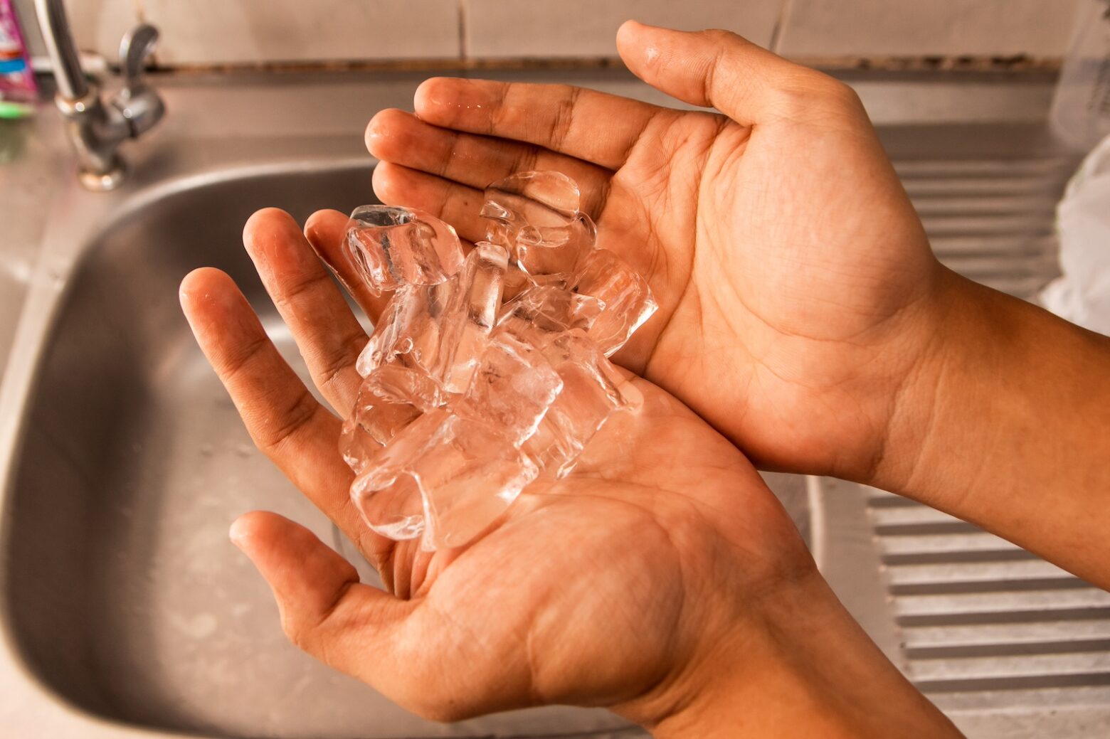 person holding ice in hands over the sink