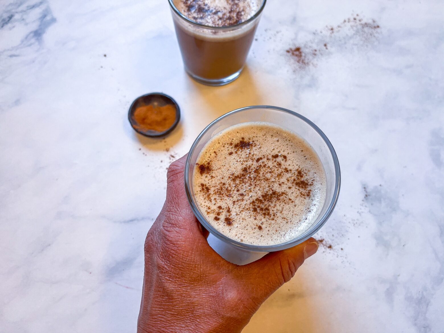 Cacao reishi latte in a glass with a hand around it.