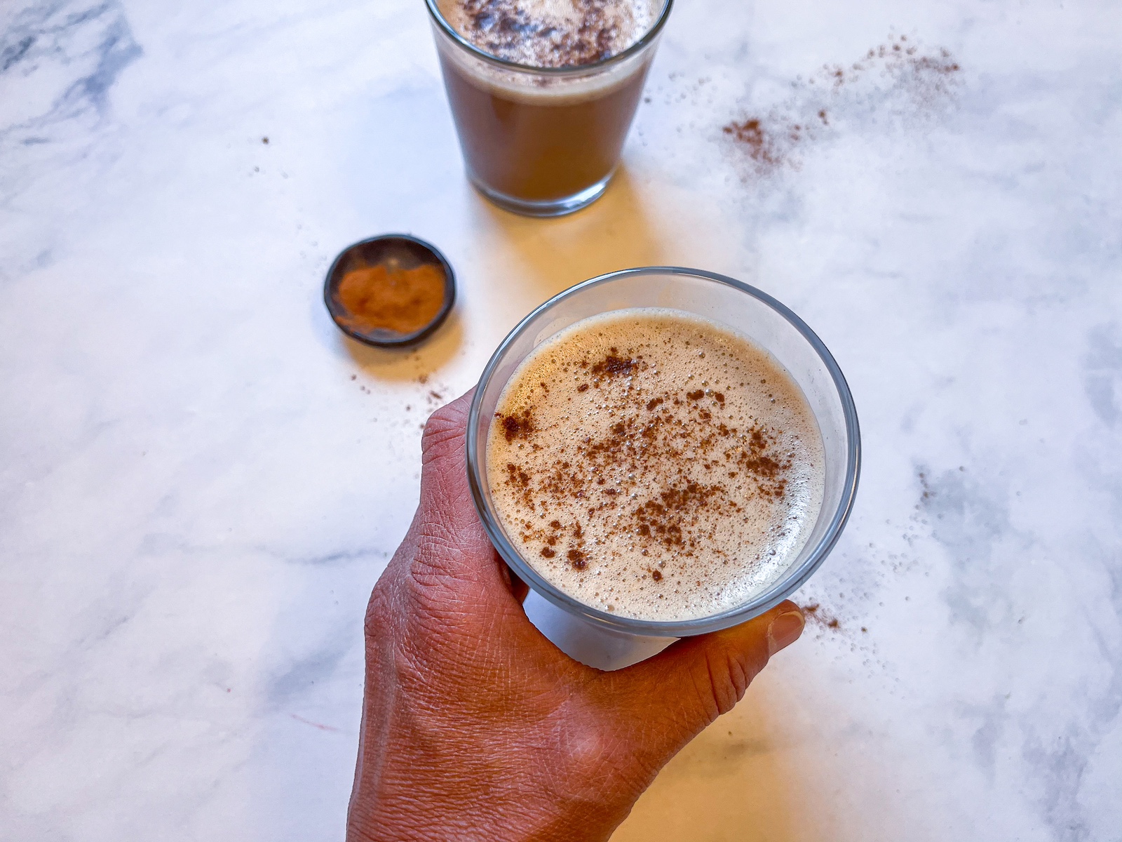 Cacao reishi latte in a glass with a hand around it.