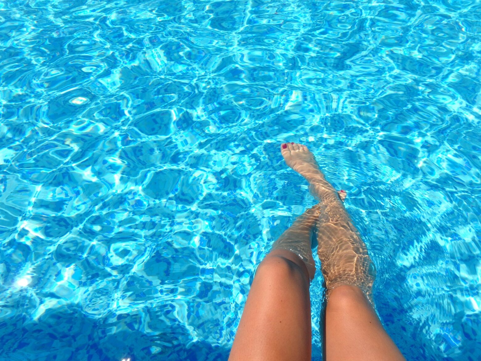 Woman sitting at the poolside, dipping her toes in the water.
