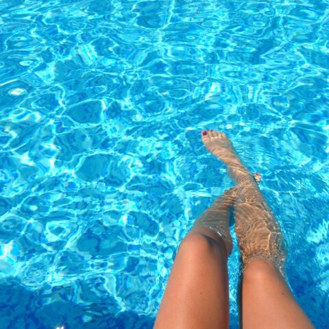 Woman sitting at the poolside, dipping her toes in the water.