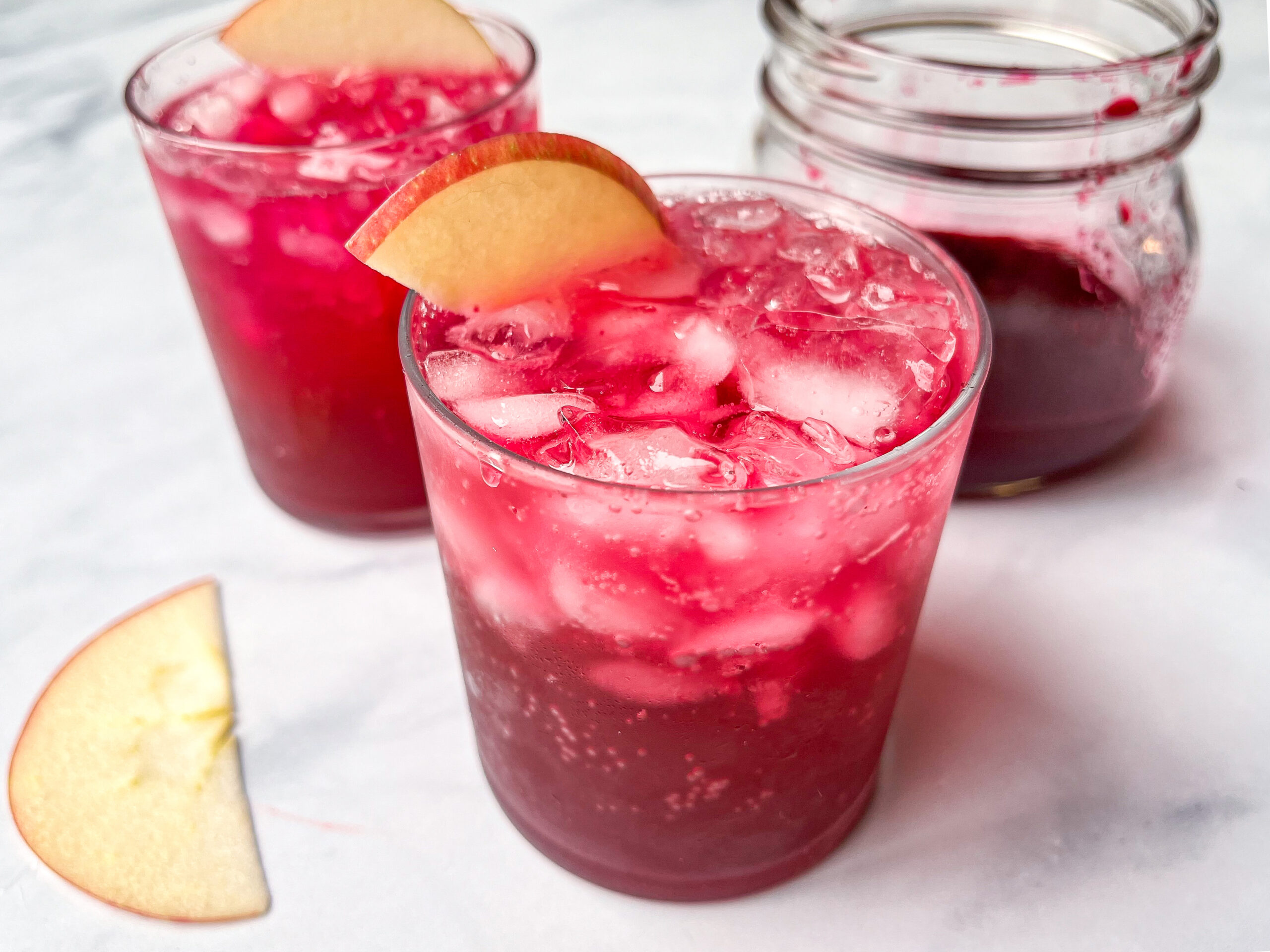 Red drink in glass with apple slice garnish.