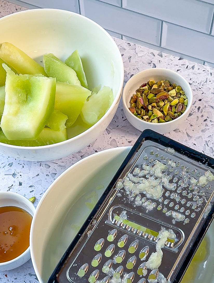 Prep photo of grating honeydew melon with melon, pistachios and honey in shot