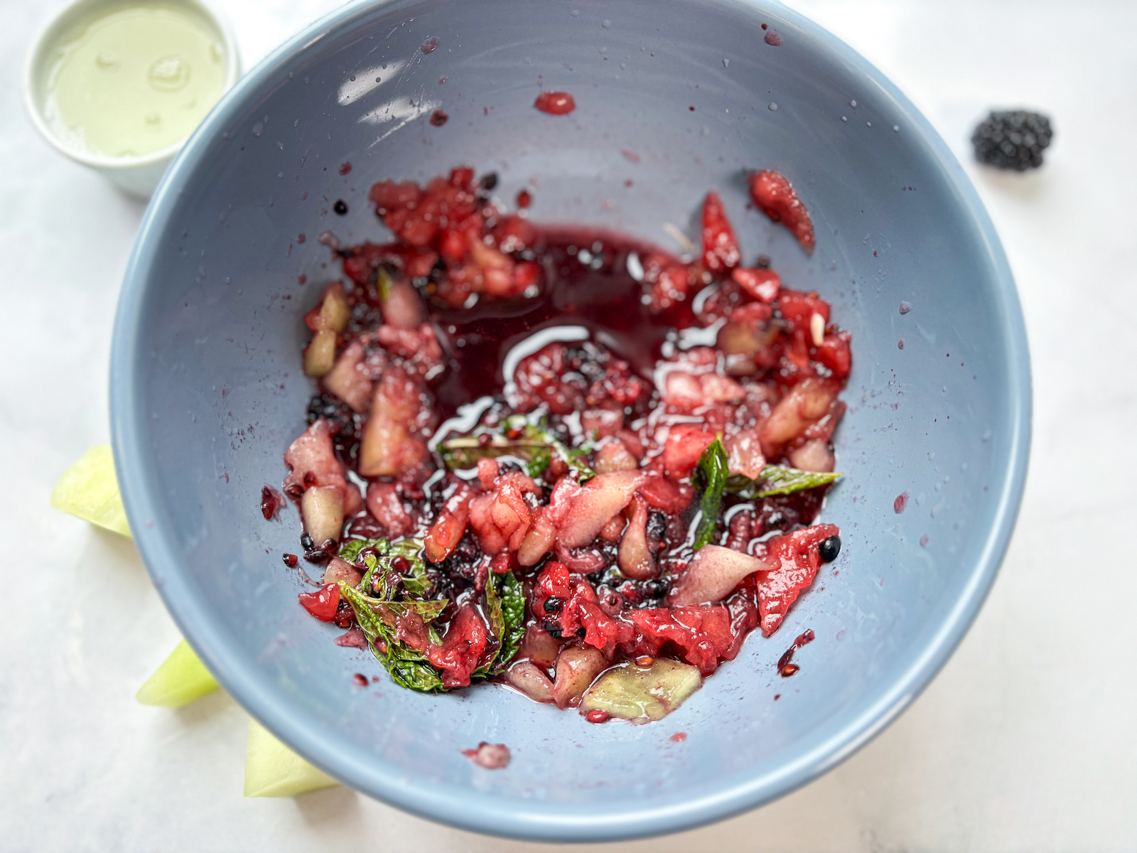 Birds eye horizontal view of mashed fruit in bowl, melon garnishes and lime juice in background