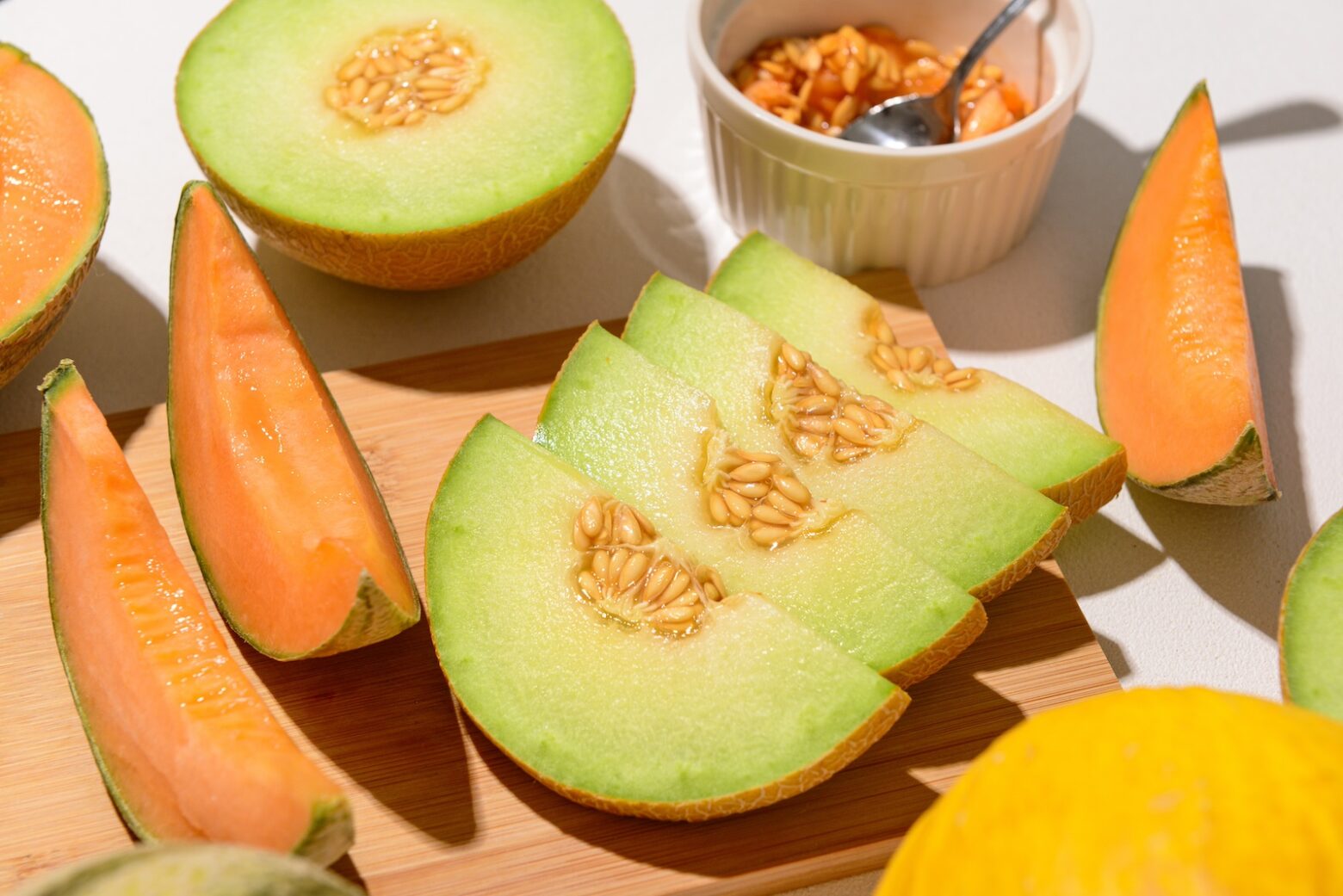 Wooden board with ripe cut melons on white background