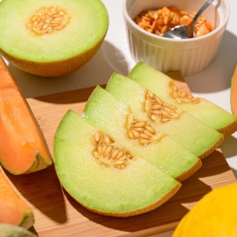 Wooden board with ripe cut melons on white background
