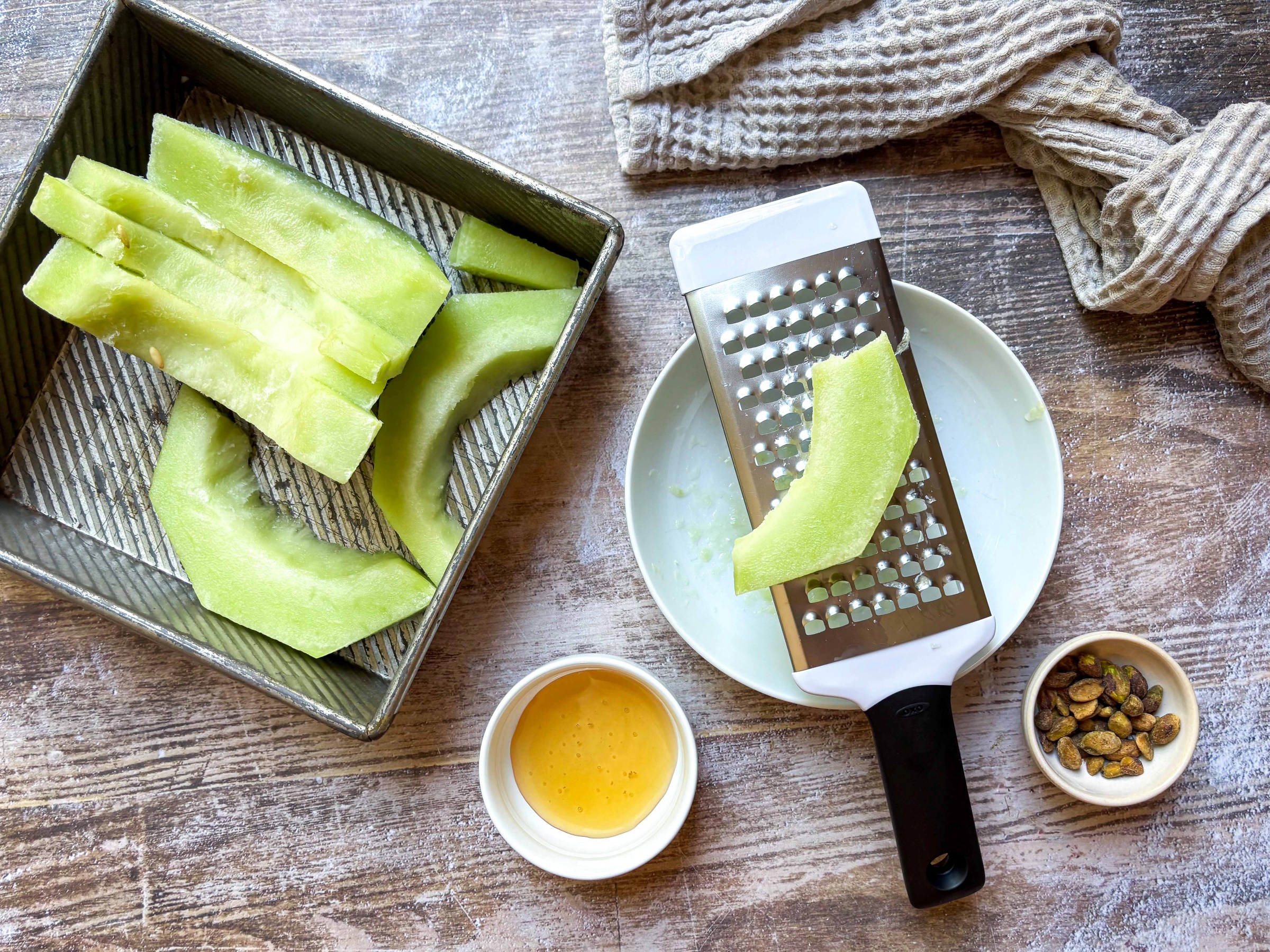 Frozen sliced honeydew shown with a microplane grater, honey, and pistachios