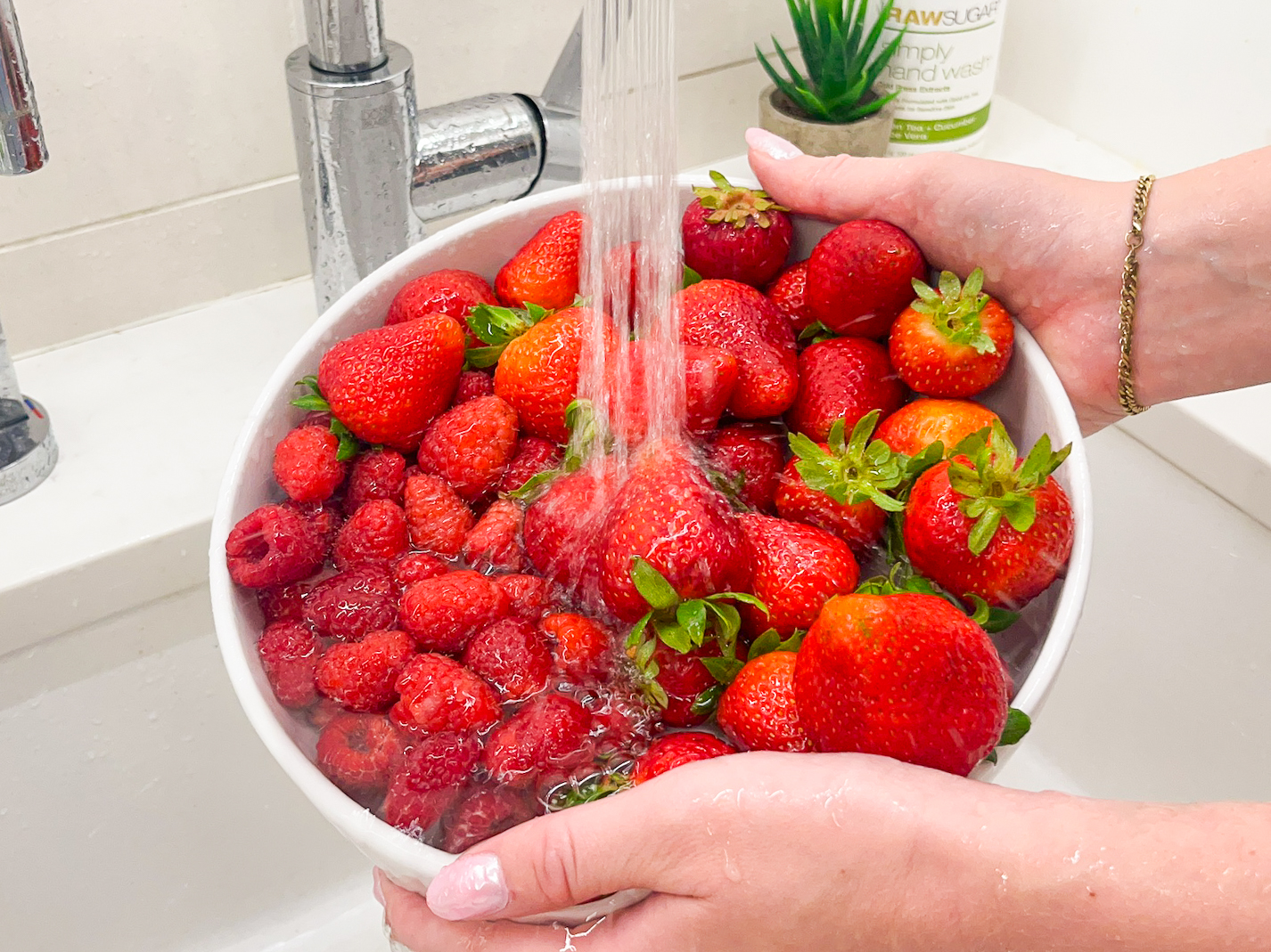 Berries being washed in the sink under water.