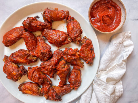 Birdseye view of finished Buffalo Beet BBQ Sauce Wings on a full plate with a dish of extra sauce and a towel next to the plate