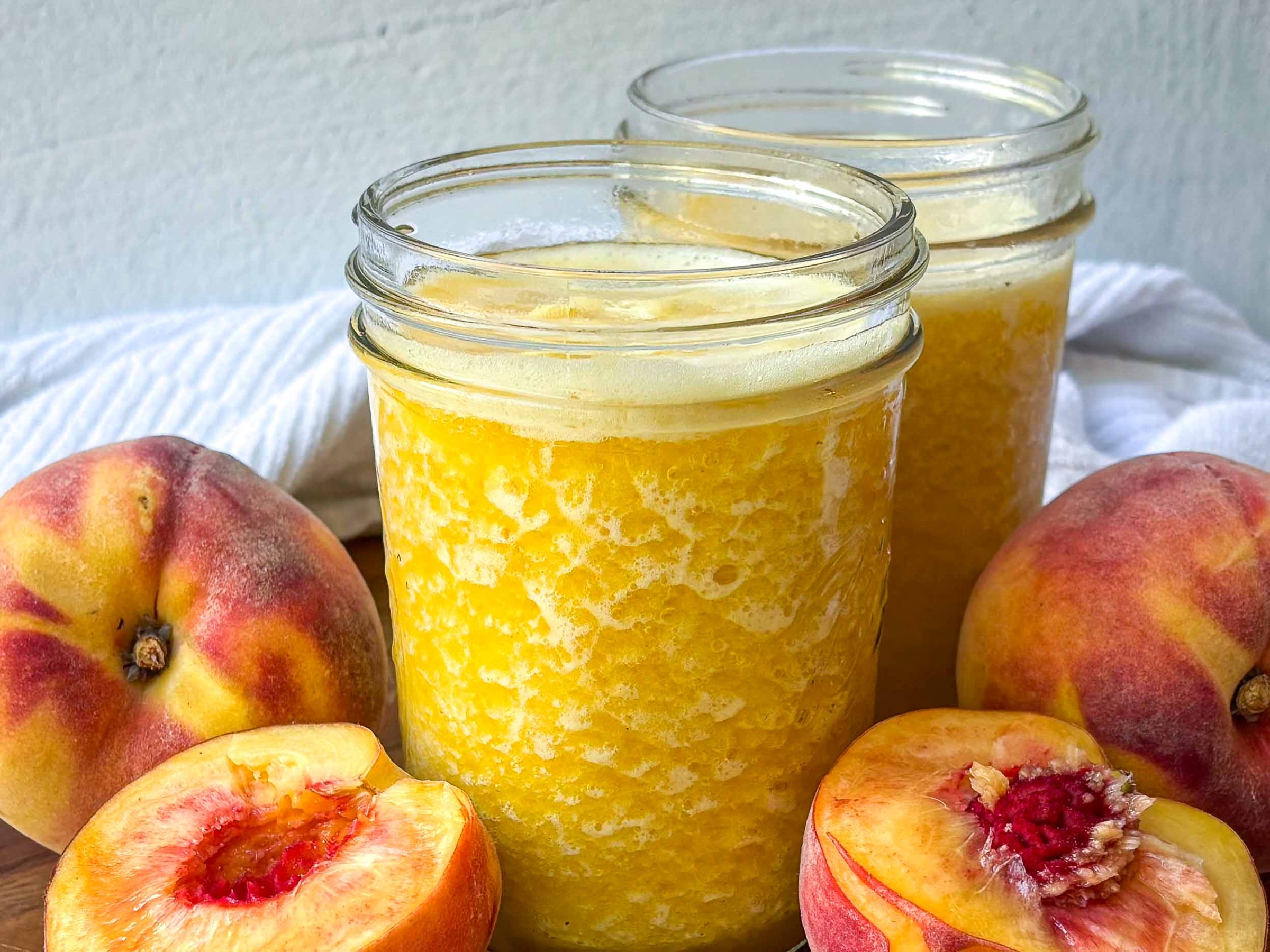 Frozen Peach Green Tea in mason jars, surrounded by fresh peaches.