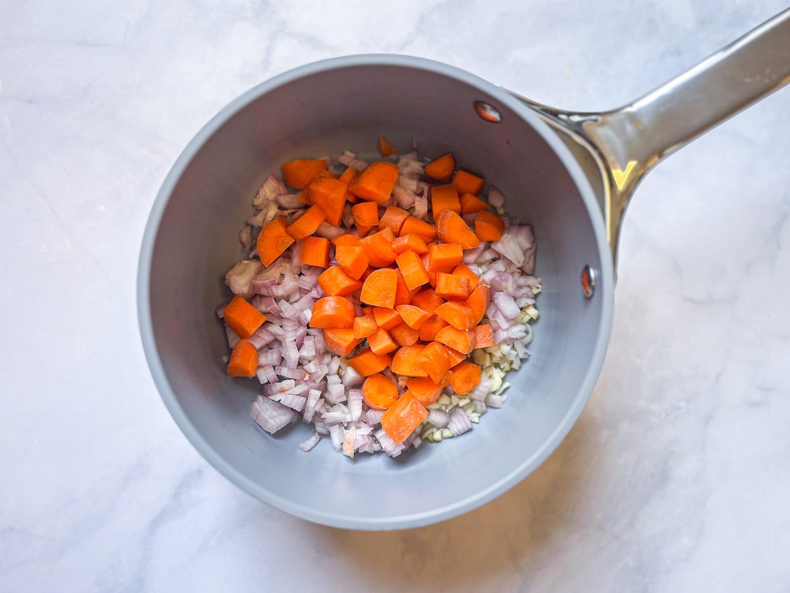 Birds eye view of shallots, carrot, and garlic in sauce pan about to start the sauté. 