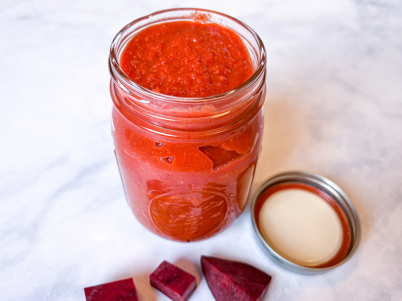 Finished jar full of buffalo beet barbecue sauce with cap off and garnish of beets