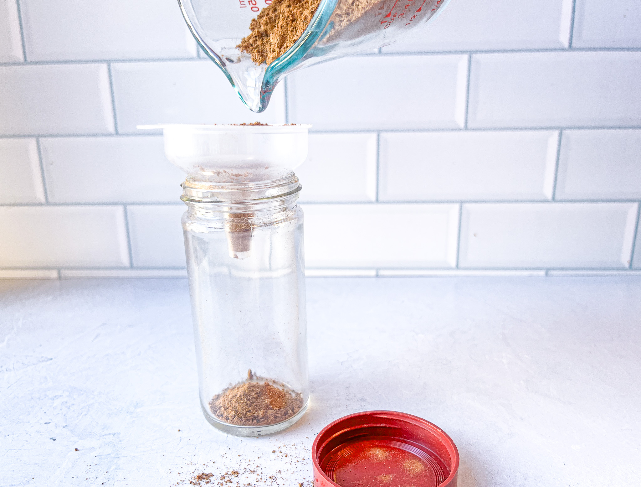 Apple pie spice being funneled into a glass spice jar.