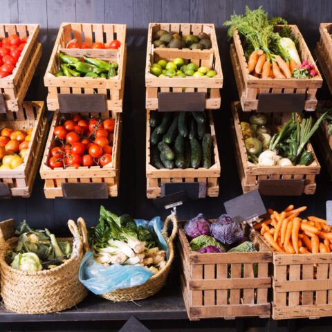 A produce stand with various fruits and vegetables each in a wooden crate or woven basket