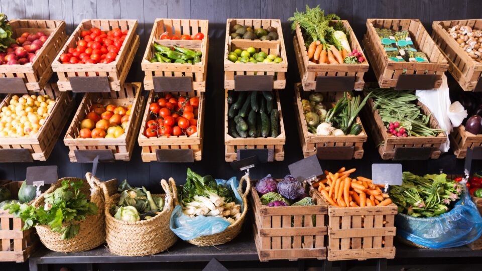 A produce stand with various fruits and vegetables each in a wooden crate or woven basket