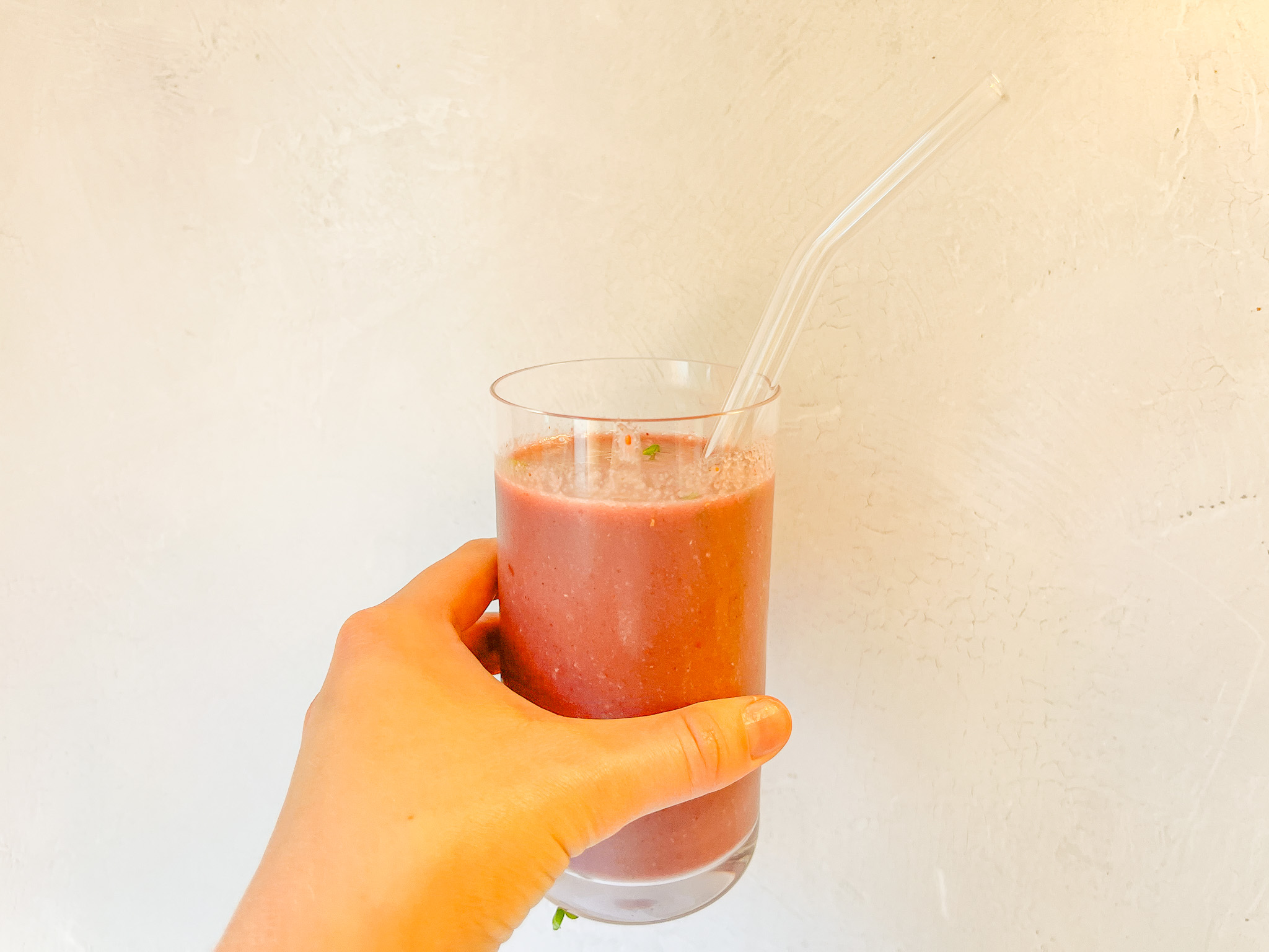 Berry Broccoli Smoothie being held with a glass straw.