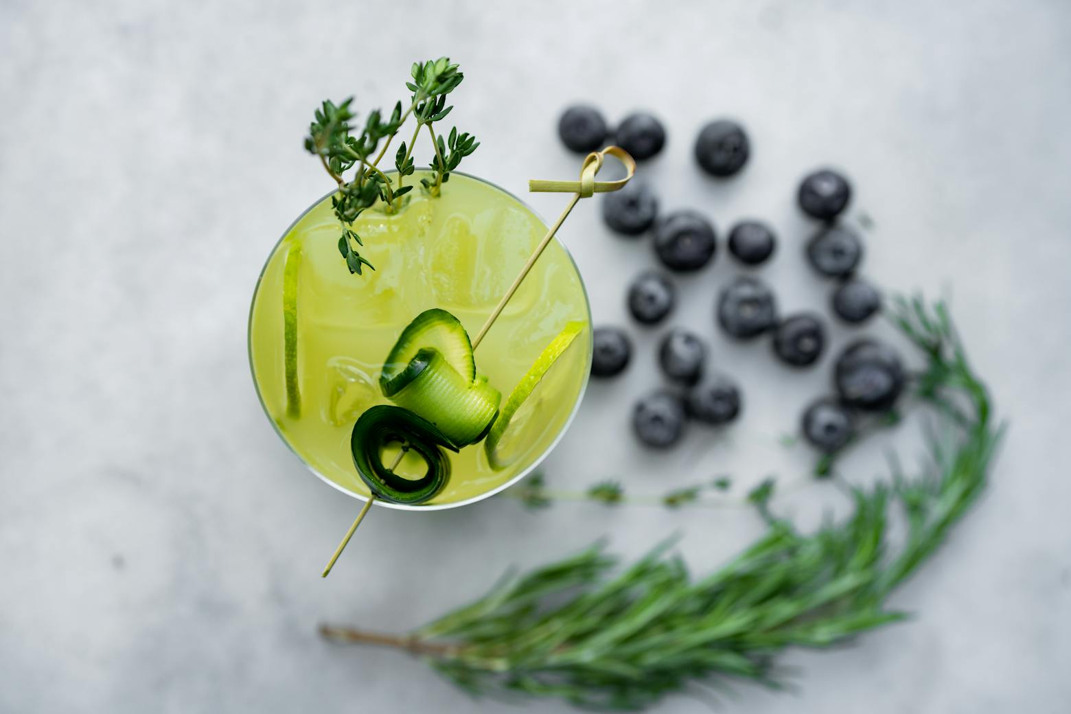 A cocktail with blueberries and herbs on a white background.