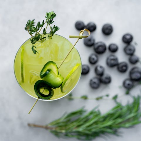 A cocktail with blueberries and herbs on a white background.