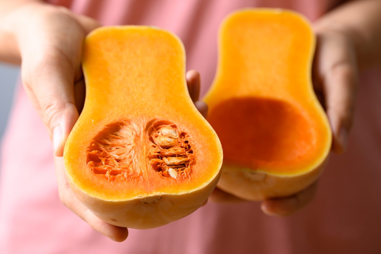 Woman displaying a halved butternut squash with the seeds still inside