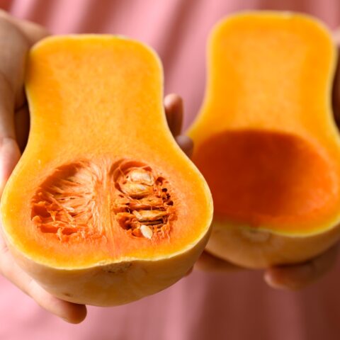 Woman displaying a halved butternut squash with the seeds still inside