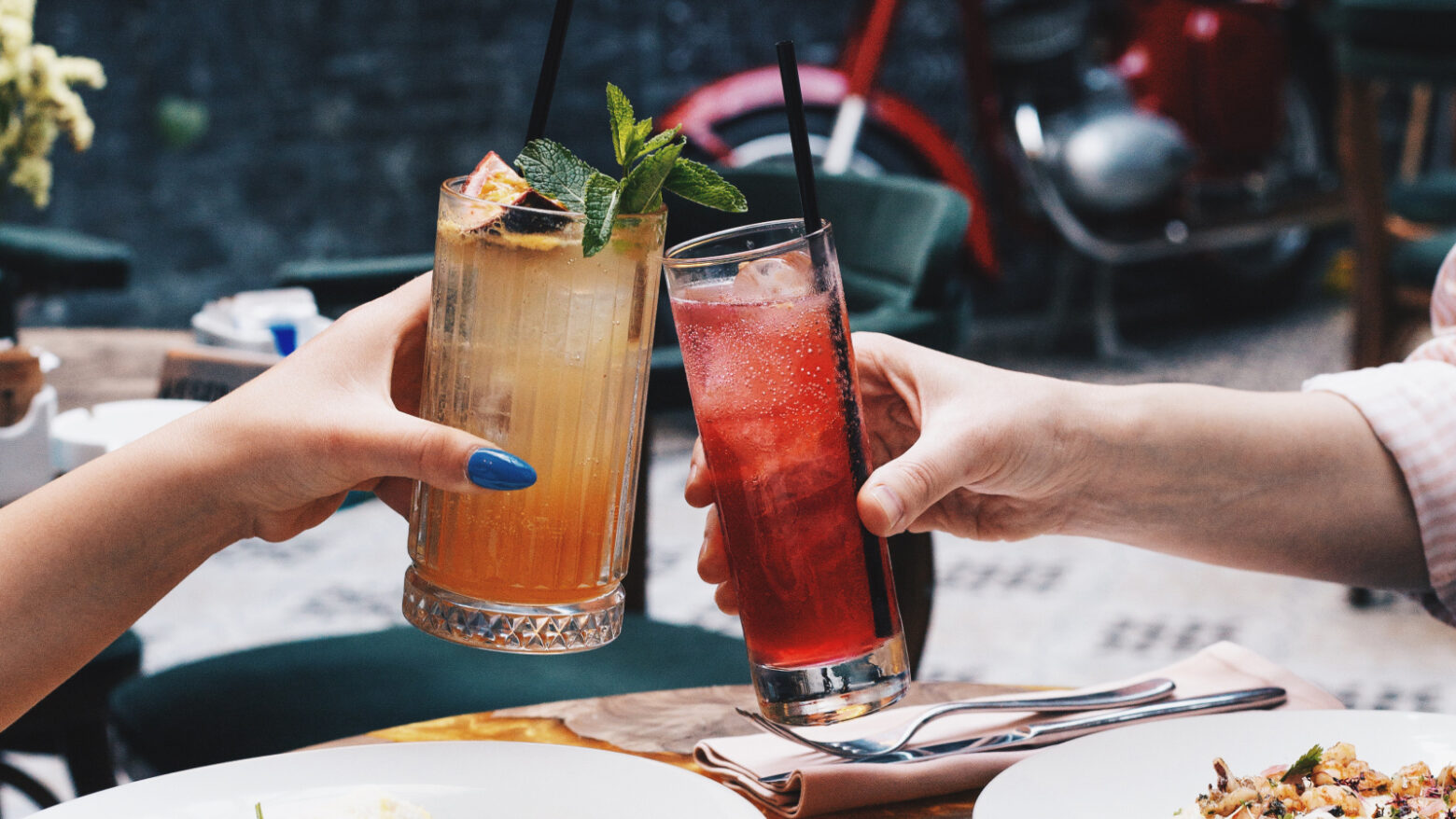 Close up of two people cheering with glasses of colorful drinks over a meal