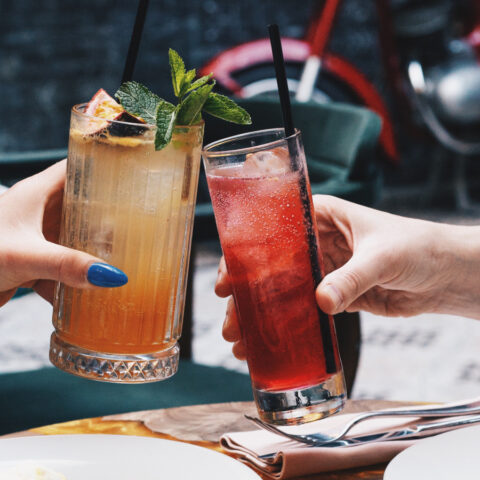 Close up of two people cheering with glasses of colorful drinks over a meal