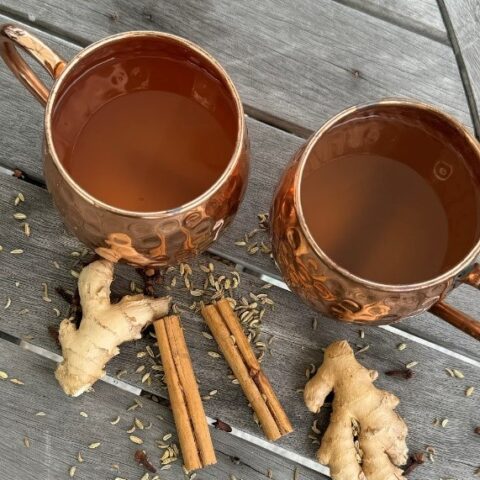 Two mugs of ginger-cinnamon tisane with whole ingredients on a wooden table