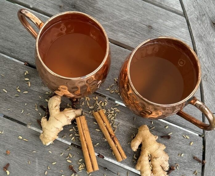 Two mugs of ginger-cinnamon tisane with whole ingredients on a wooden table