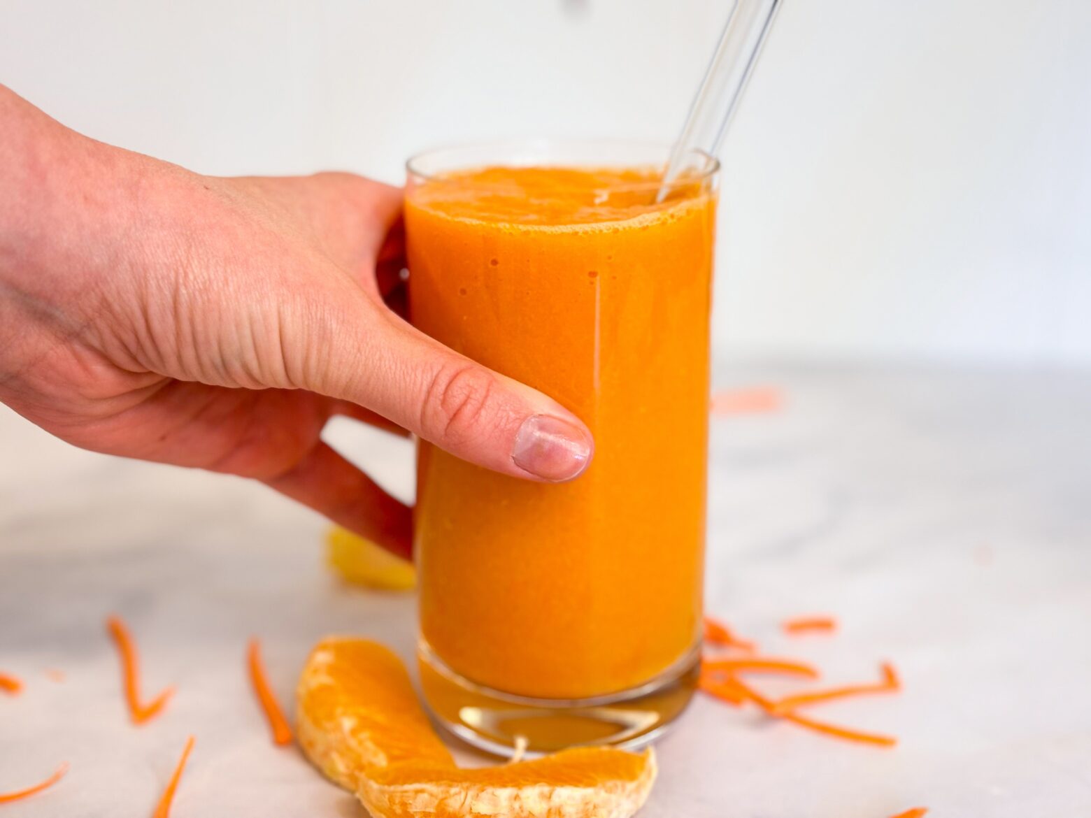 Carrot smoothie with a hand in it and a straw.