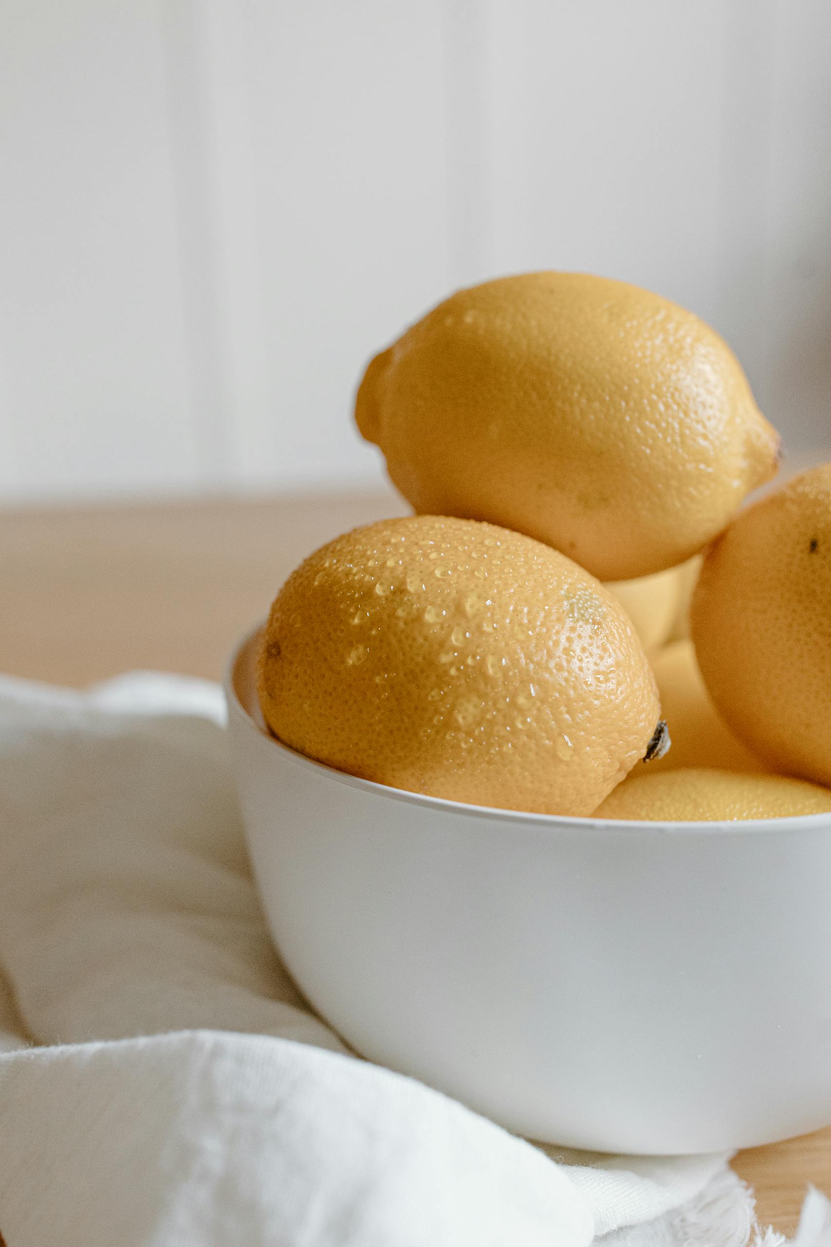 A bowl of fresh lemons on a wooden table.