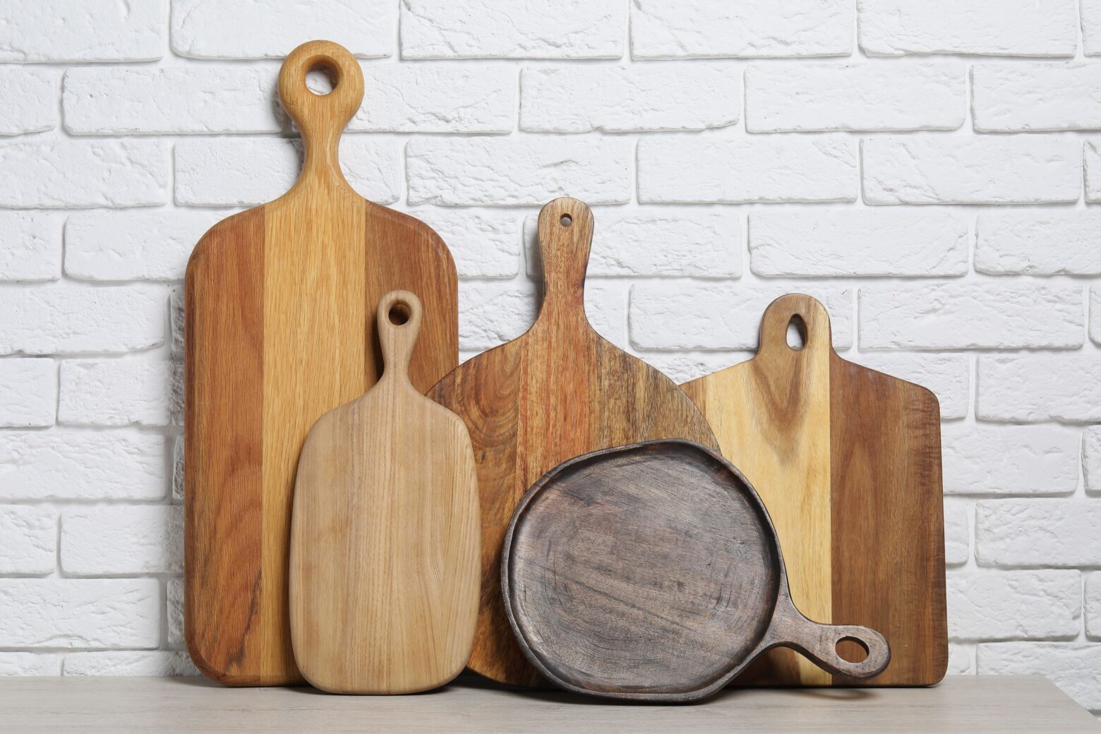 A variety of wooden cutting boards against a white brick wall