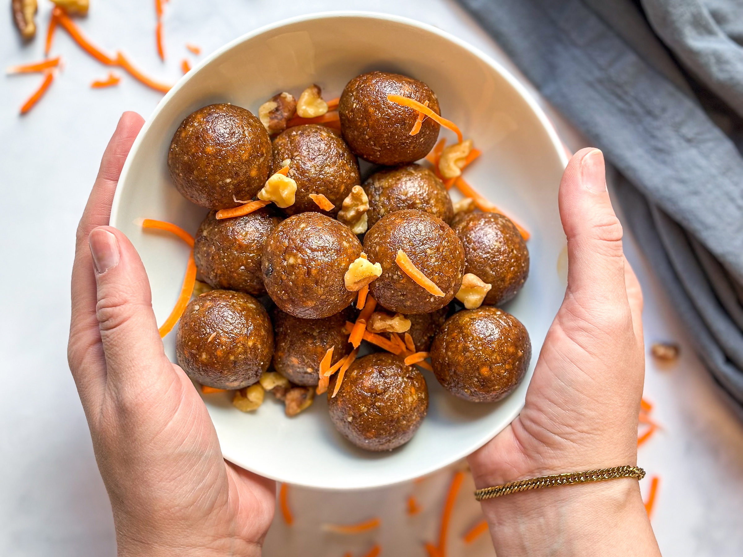 No-bake carrot cake energy balls in a bowl with hands, finished. 