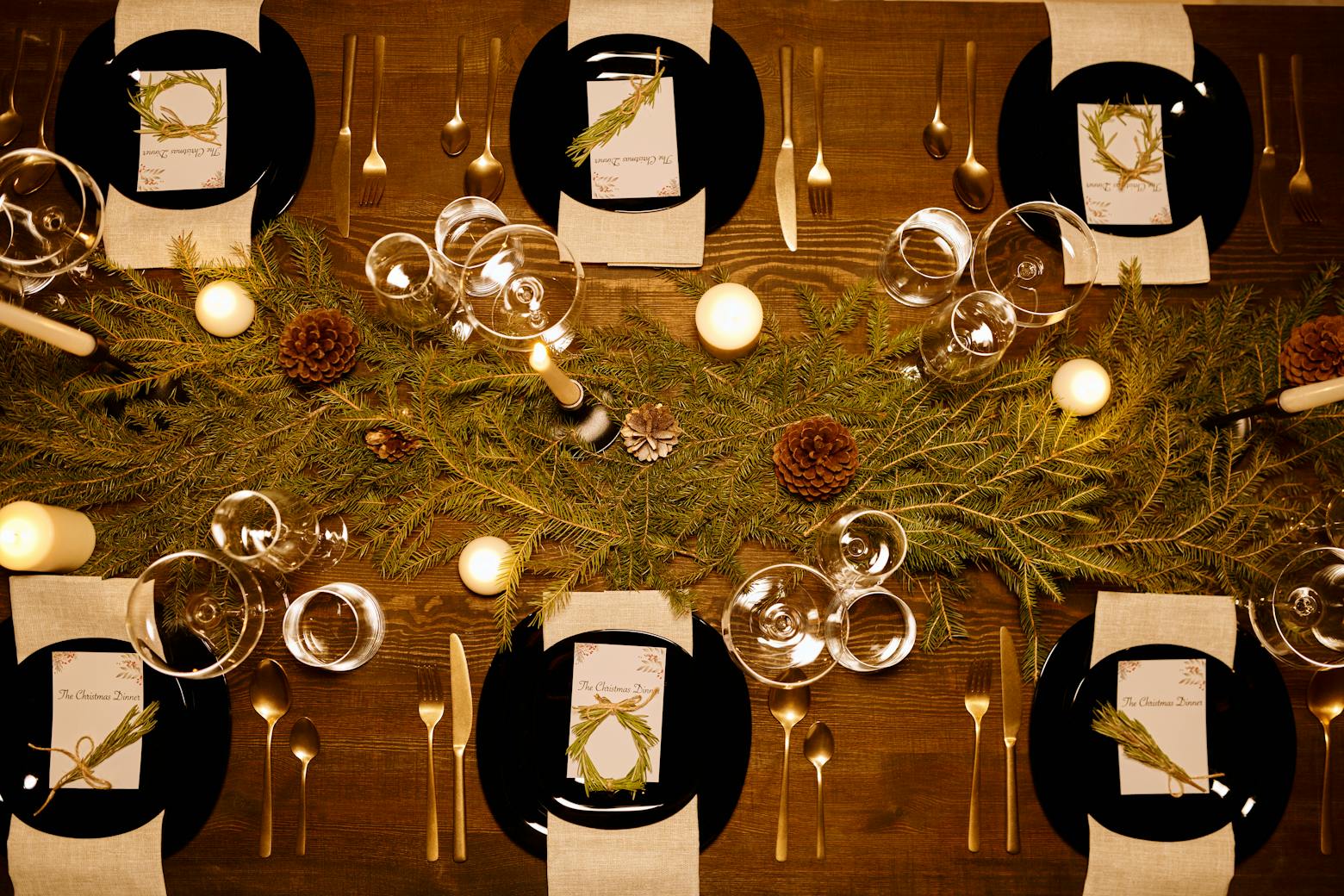 Elegant Christmas dinner table with candles, pine decor, and luxury dinnerware.