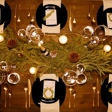 Elegant Christmas dinner table with candles, pine decor, and luxury dinnerware.