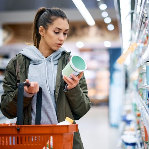 A woman reads the label of a dairy product while shopping for groceries.