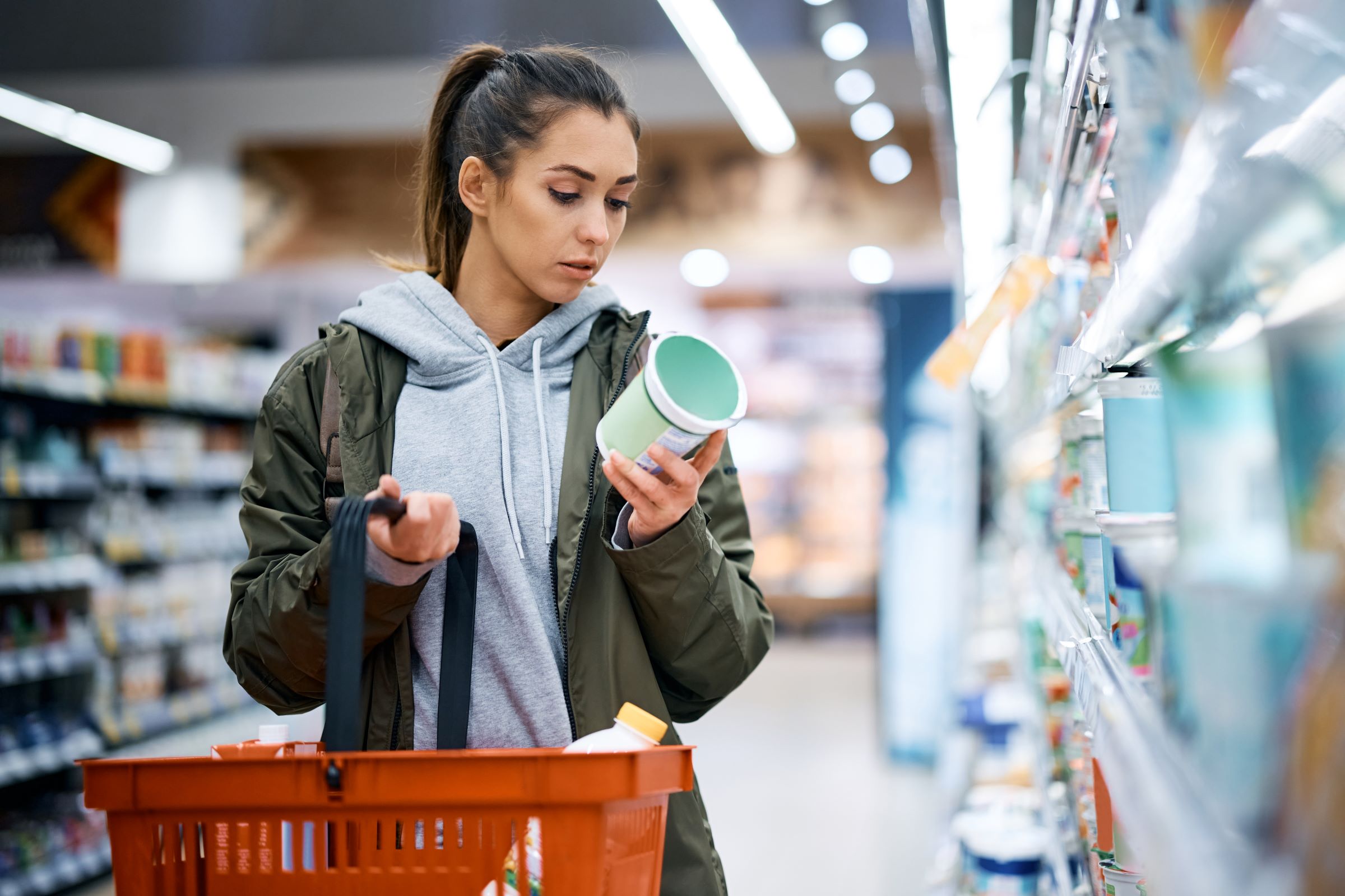 A woman reads the label of a dairy product while shopping for groceries.